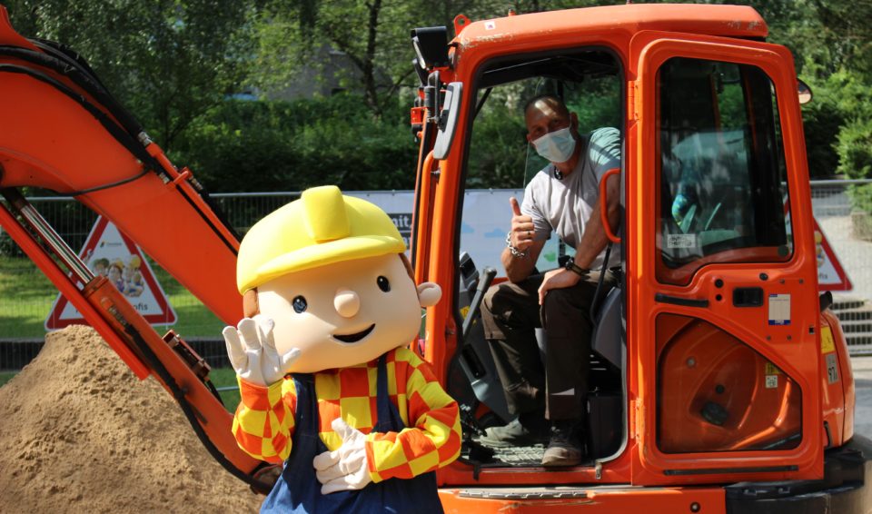 Bob der Baumeister posiert mit unserem Mitarbeiter aus der Gartenabteilung vor dem Bagger